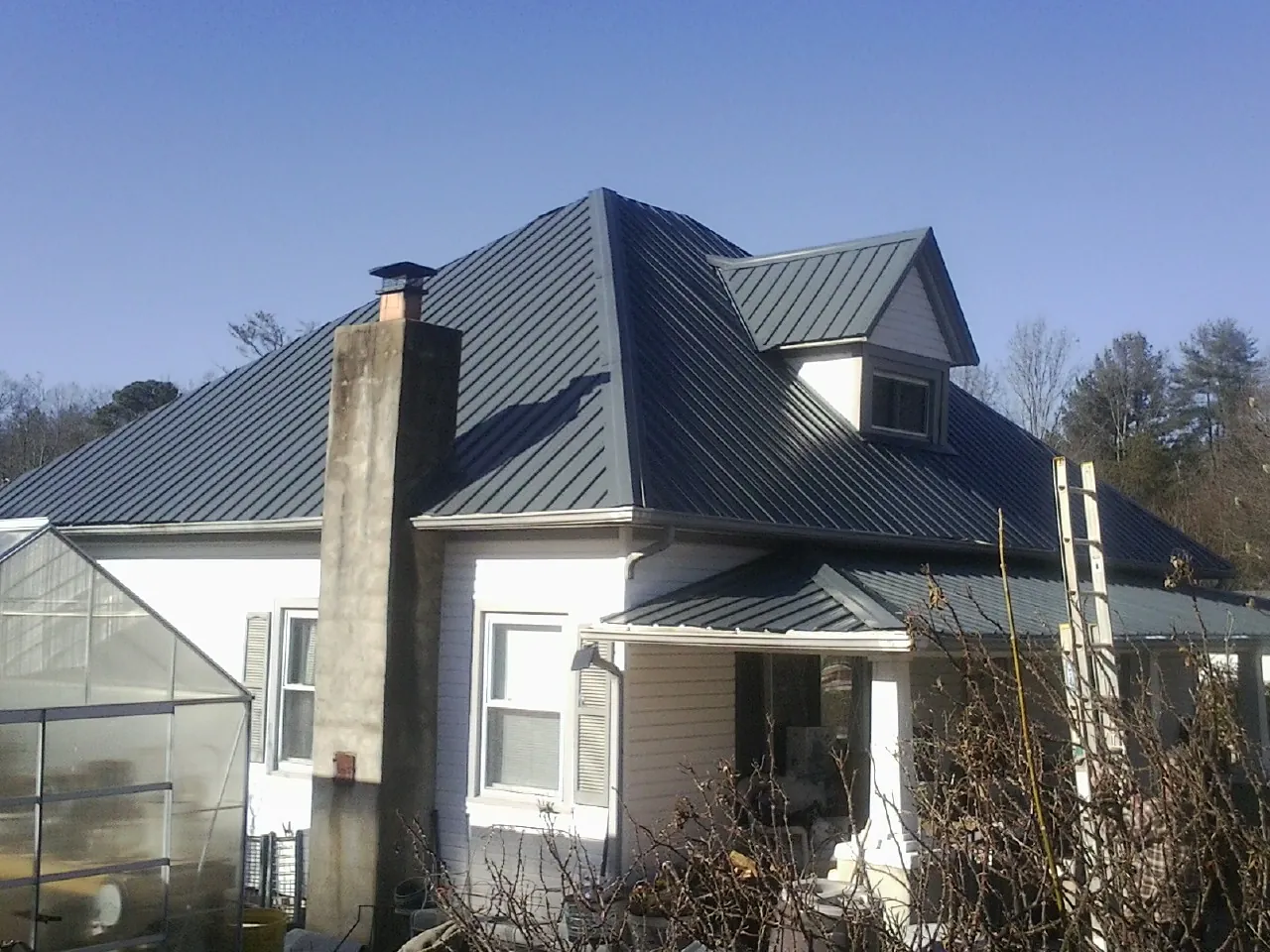 Dark blue standing seam metal roof on a white farmhouse with dormer in Wagener