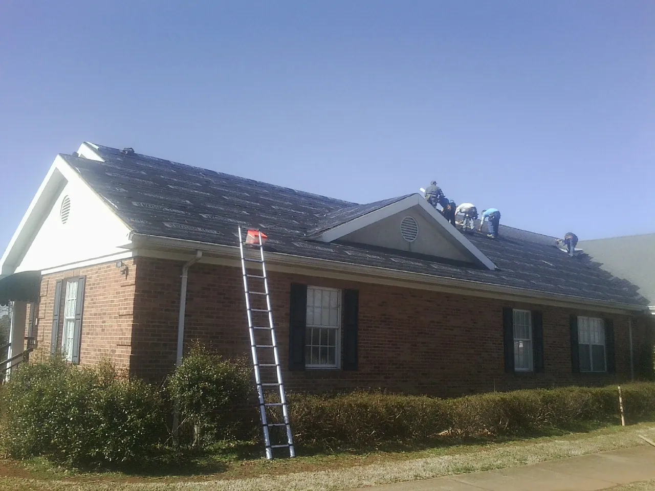 Crew tearing shingles off a brick ranch roof with a ladder set — Emergency Roof Repair work by our crew in Wagener