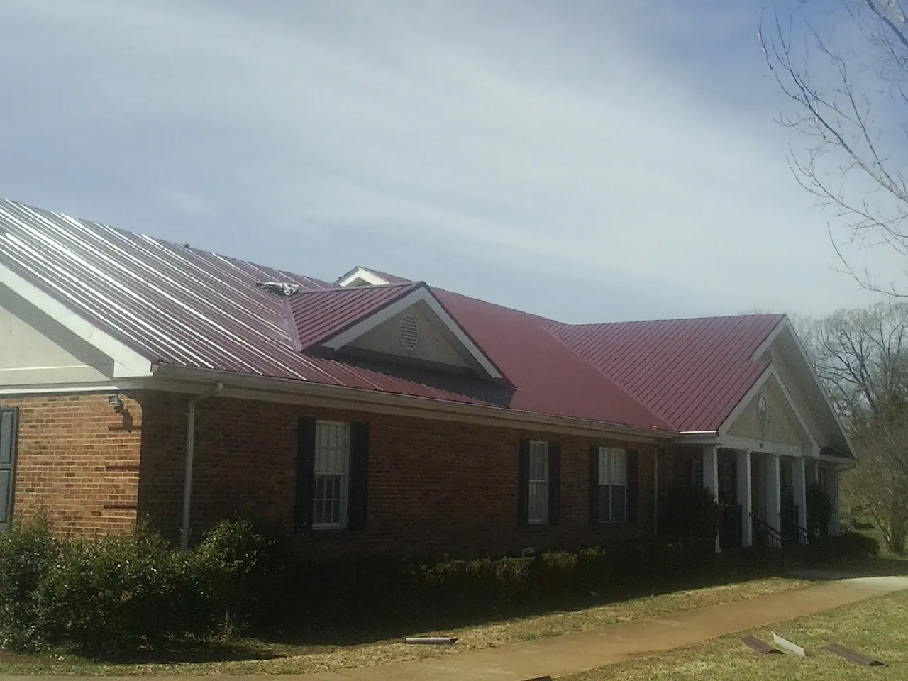 Red metal roof with gabled entries on a long brick building, from a Hail Damage Roof Repair job in Wagener