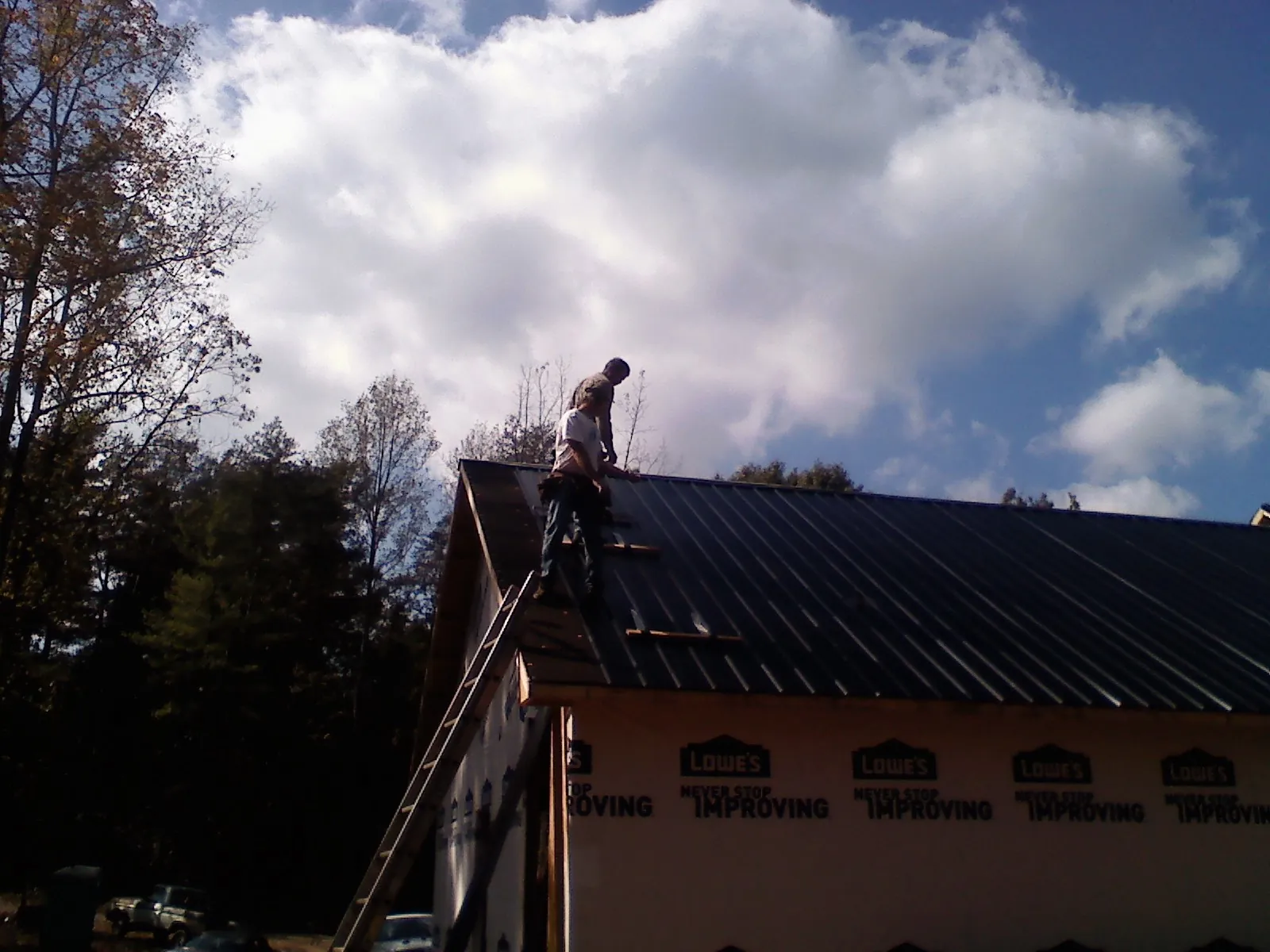 Roofer fastening dark metal panels high against a cloudy sky, from a Roof Inspection job in Wagener