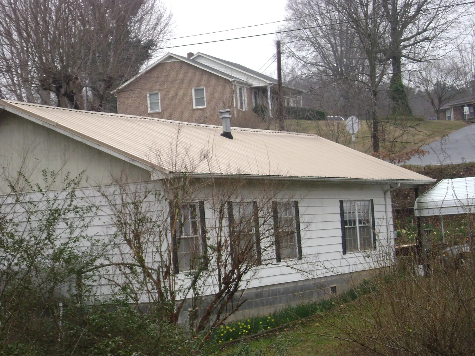 Tan metal roof on a white sided house set into a hillside — Commercial Roofing by Roofing Brothers in Wagener